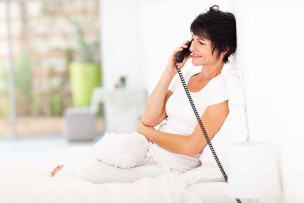 ベッドの上で固定電話で話をしている女性